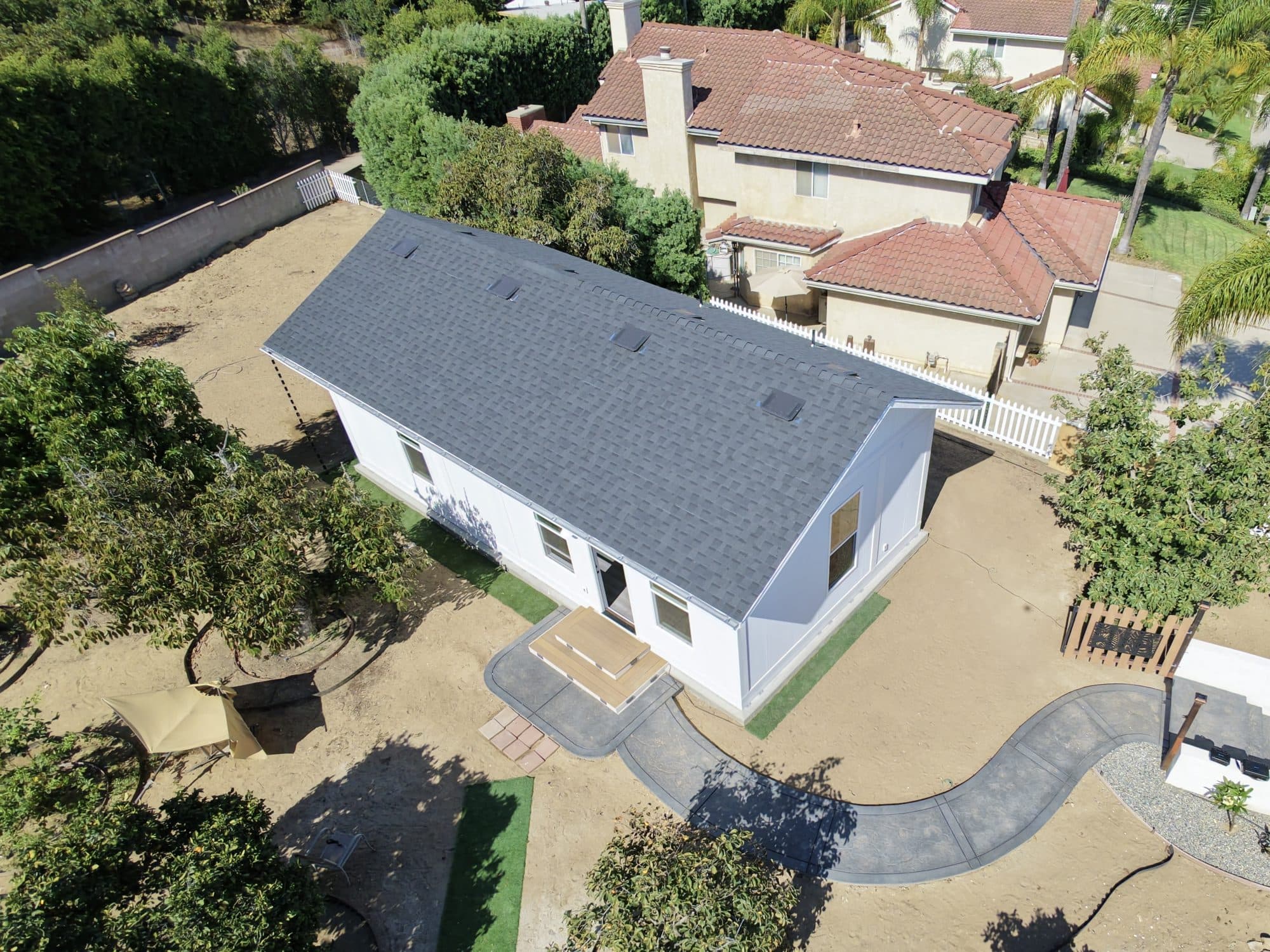 Aerial view of a Boxabl Casita in a Southern California backyard with a site-built gray shingle gable roof, entry steps, and a curving concrete path