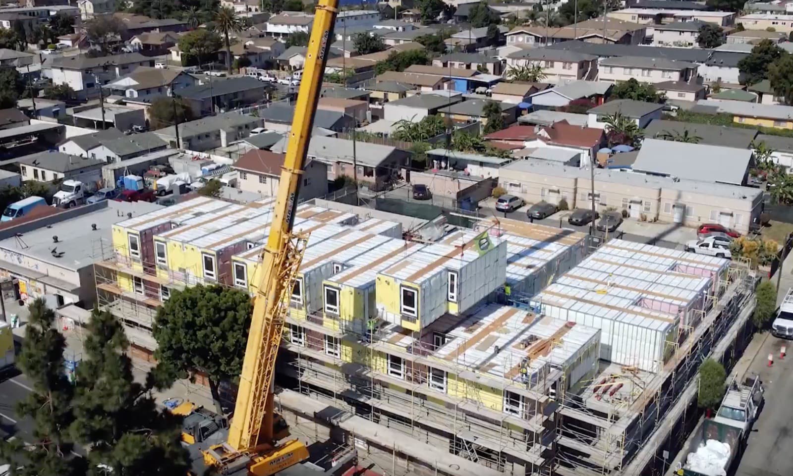 A steel building module being lifted by crane onto a multifamily job site